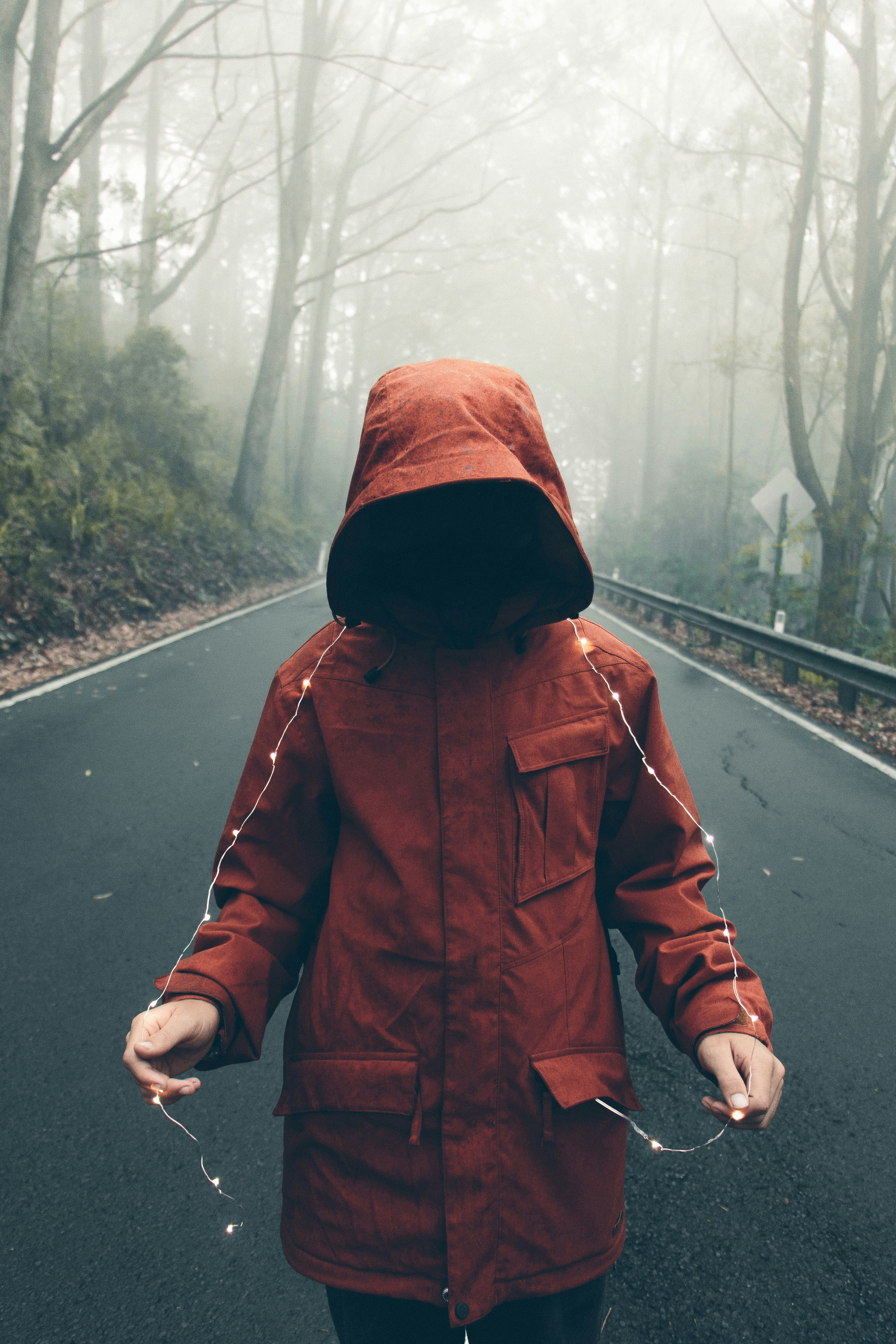 person in red hooded jacket holding string lights